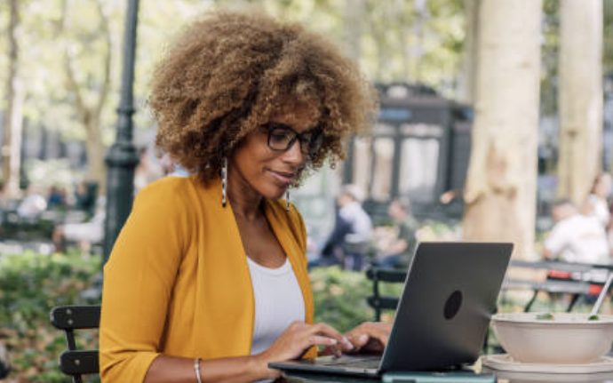 A woman typing on a laptop at a café table in a park